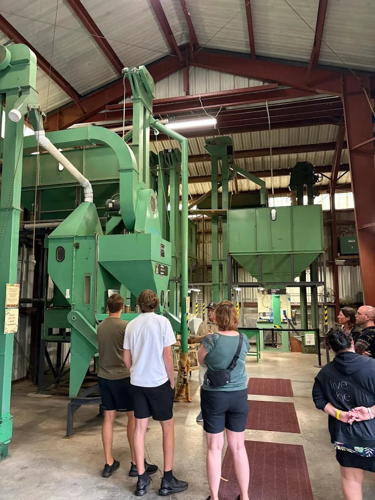 Group of people observing large green industrial machinery in a warehouse setting