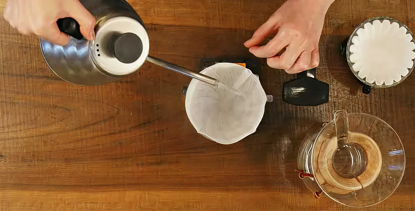 Person making coffee using a pour-over method on a wooden surface